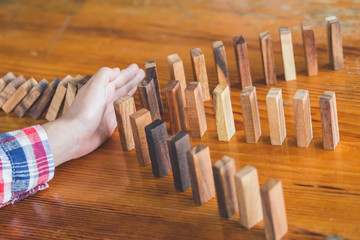  Businessman hand stopping falling wooden dominoes effect from continuous toppled or risk, strategy...