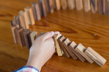  Businessman hand stopping falling wooden dominoes effect from continuous toppled or risk, strategy...