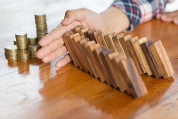  Businessman hand stopping falling wooden dominoes effect from continuous toppled or risk, strategy...