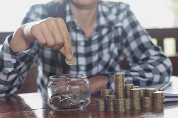Woman's hand putting coin into glass of bottle for saving money, Saving money concept