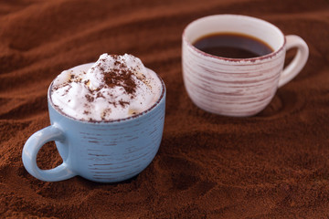 Closeup of tasty coffee and whipped cream. Cups on a table covered with ground coffee.