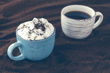 Closeup of tasty coffee and whipped cream. Cups on a table covered with ground coffee. Fog filter effect