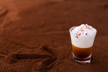 Little cup of piccolo latte macchiato on a table covered with arrow on ground coffee as a background