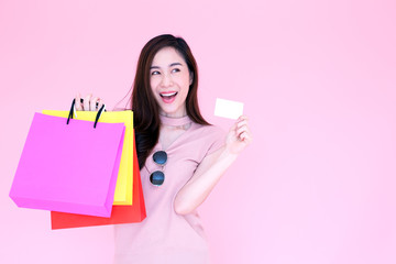 Beautiful asian women are shopping in the Valentine week, Happy pretty girl enjoys using a credit card and holding shopping bags in discount and sale festival isolated over pink background