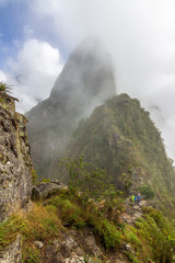 Huayna Picchu appear in front of our eye in between the fog while the clouds retreat. Steep walls with impressive valleys and mountains surround the old city of the Inca Empire, Peru, South America