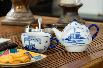 A porcelain teapot and a cup with sugar and cookies on a rustic coffee table, day light, indoors.