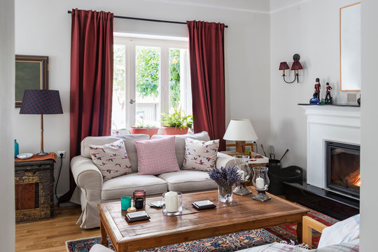 Large living room very bight  with fireplace, oak wooden floor, red curtins, a trunk and retro objets, Greece.