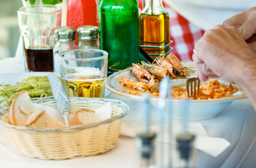 A man hand having lunch with shrimp, green pasta and beer outdoors in Mykonos, Greece.