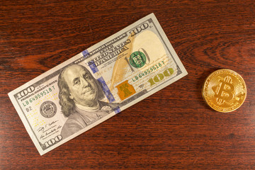 Bitcoin coin lies on a 100 banknote on the table