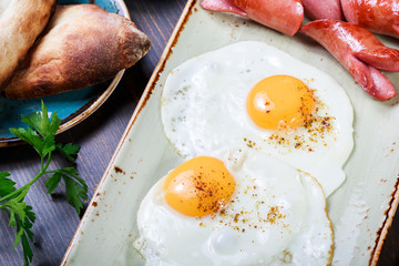 Fried eggs and sausage with bread and fresh vegetables. Hot and healthy breakfast, top view, flat lay