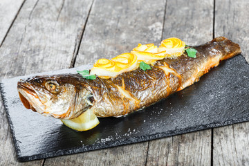 Grilled sea fish with lemon on stone slate background close up. Healthy food. Top view