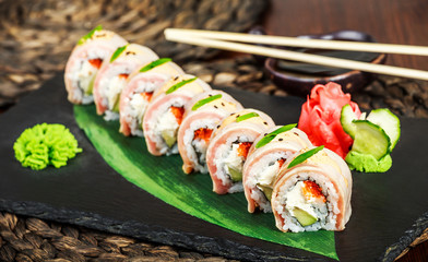 Sushi rolls set with salmon, cream cheese, red caviar, avocado and wasabi on black stone on bamboo mat, selective focus. Japanese cuisine