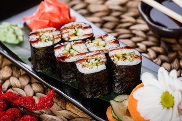 Sushi Roll - Maki Sushi with Smoked Eel, cucumber and avocado on black stone on bamboo mat decorated with flowers. Japanese cuisine