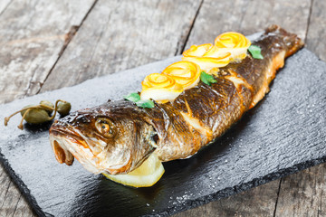 Grilled sea fish with lemon on stone slate background close up. Healthy food. Top view
