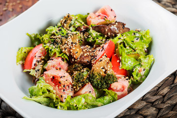 Warm salad with chicken liver, tomatoes, lettuce leaves, broccoli on wooden table. Healthy food. Top view