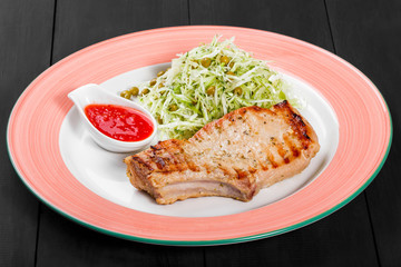 Grilled pork steak with green salad of cabbage and peas in plate on dark background. Hot Meat Dishes. Top view, flat lay