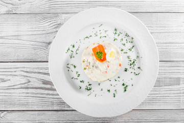 Traditional russian Christmas and New year salad Olivier with decoration on the plate on light wooden. Top view