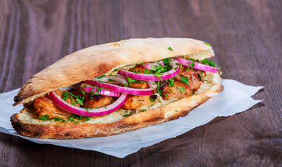 Grilled chicken in sandwich from fresh pita bread with onion and greens on dark wooden background....