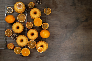 Fototapeta na wymiar Small orange Bundt cakes with fresh and dry oranges on cooling ruck, top view, flat lay, copy space