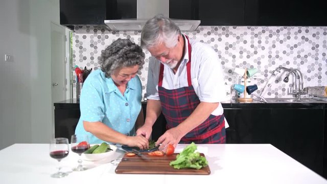 Senior couple preparing food in kitchen. Retired old Asian male and female, preparing salad in kitchen together, happy smile. Senior lifestyle concept.