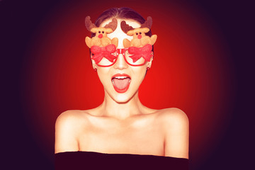 Beautiful stylish girl in black outfit celebrating christmas. Girl in funny  glasses with new year's deer and bows. Model smile, happy in red background. Happy new year 2019. Excited woman. © MoreThanProd