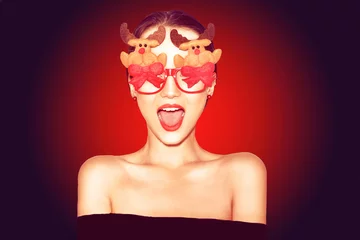 Beautiful stylish girl in black outfit celebrating christmas. Girl in funny  glasses with new year's deer and bows. Model smile, happy in red background. Happy new year 2019. Excited woman. © MoreThanProd