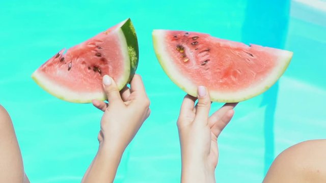 Womens hands simultaneously moving watermelon slices against swimming pool