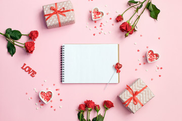 Open blank notebook with gift box, flowers and hearts on a pink background. Valentines day background.