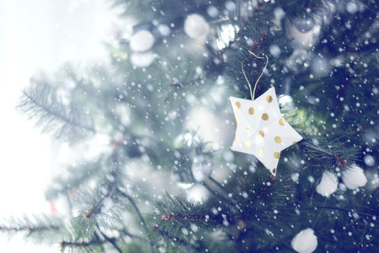 Silver star hanging from a decorated Christmas tree with bokeh and snow, copy space. Xmas holiday background.