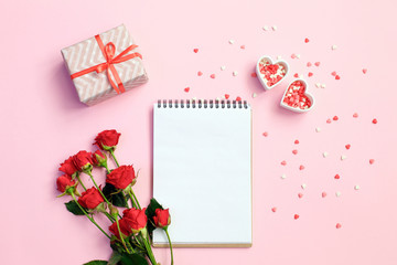 Open blank notebook with gift box, flowers and hearts on a pink background. Valentines day background.