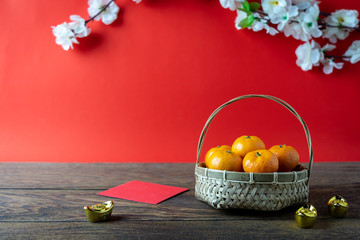 Accessories on Lunar New Year & Chinese New Year vacation concept background.Orange in wood basket with  red pocket money and flower on modern rustic brown & red backdrop at home office desk studio.