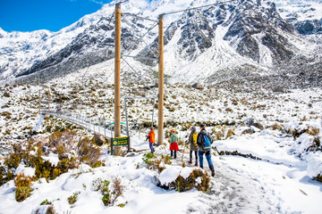 Group of people across the river by a swing bridge in Hooker Valley Track covered with white snow after a snowy day. Mount Cook National Park.