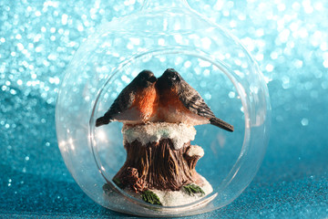 The couple of bullfinches sits on the snowy stump inside the glass transparent Christmas ball on a...