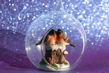 The couple of bullfinches sits on the snowy stump inside the glass transparent Christmas ball on a...