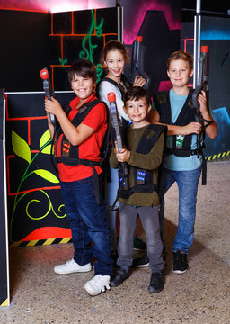 Group portrait of happy teenagers with laser guns having fun on dark lasertag arena