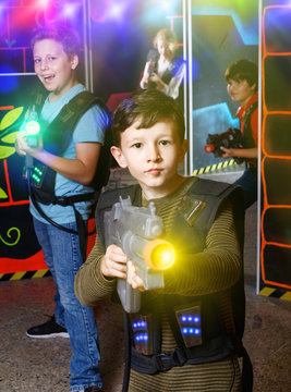 Emotional teen boy with laser pistol playing laser tag with frie