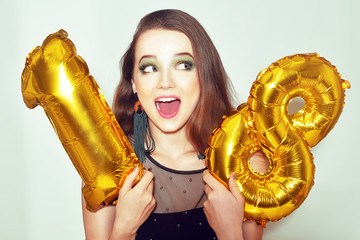 A birthday girl on her 18th birthday with gold number baloons. Excited eighteen girl with green...