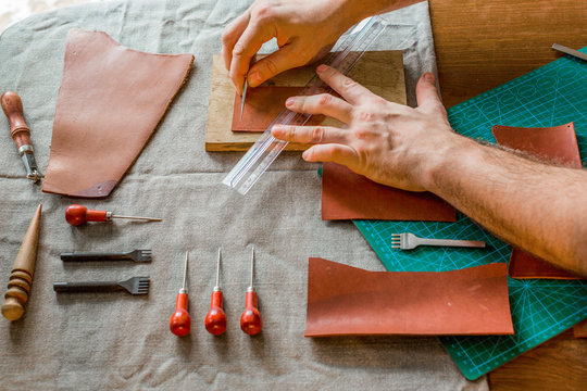 Working process of the leather bag for money or messenger in the leather workshop by master craftsman hands on the table background. Color tone image