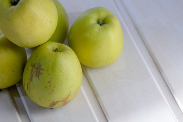 Many green apples on a shelf. A white, wooden background.