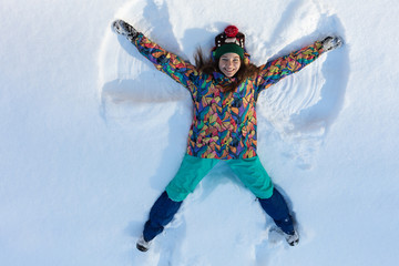 High angle view of happy girl lying on snow and moving her arms and legs up and down creating a...