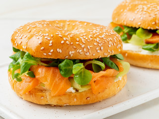 Two sandwiches with salmon, cream cheese, cucumber slices on white marble table