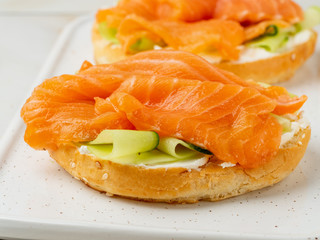 Two open sandwiches with salmon, cream cheese, cucumber slices on white marble table, close up