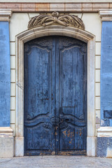 Old wooden door with peeling blue paint and carvings in the Gothic Quarter in Barcelona, Spain
