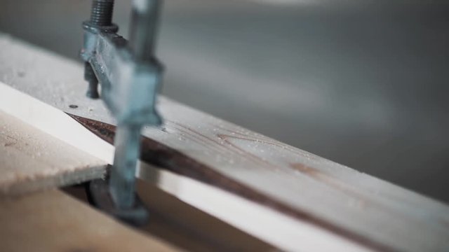 Closeup of black metallic tool with plastic handle connected to yellow wooden plank in workhouse in daylight.