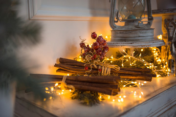 Christmas Decoration, cinnamon sticks in festive lights garland yellow. Christmas decorations are on the white fireplace.