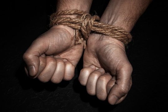 Man with hands tied with rope on black background. The concept of slavery or prisoner.