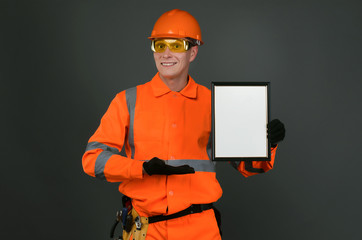 Happy builder worker in a hardhat is showing a blank certificate diploma in hands isolated on gray background.