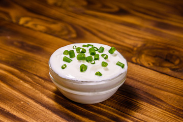 Obraz na płótnie Canvas Glass bowl with sour cream and chopped green onion on wooden table