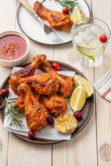 Tasty appetizing baked chicken legs served with spices, rosemary and cranberries on wooden background table. Christmas dish. Copy space.