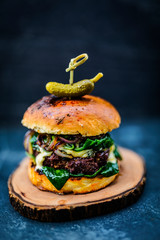 Tasty grilled beef burger with spinach lettuce and blue cheese served on wooden table with copyspace, blackboard in background.